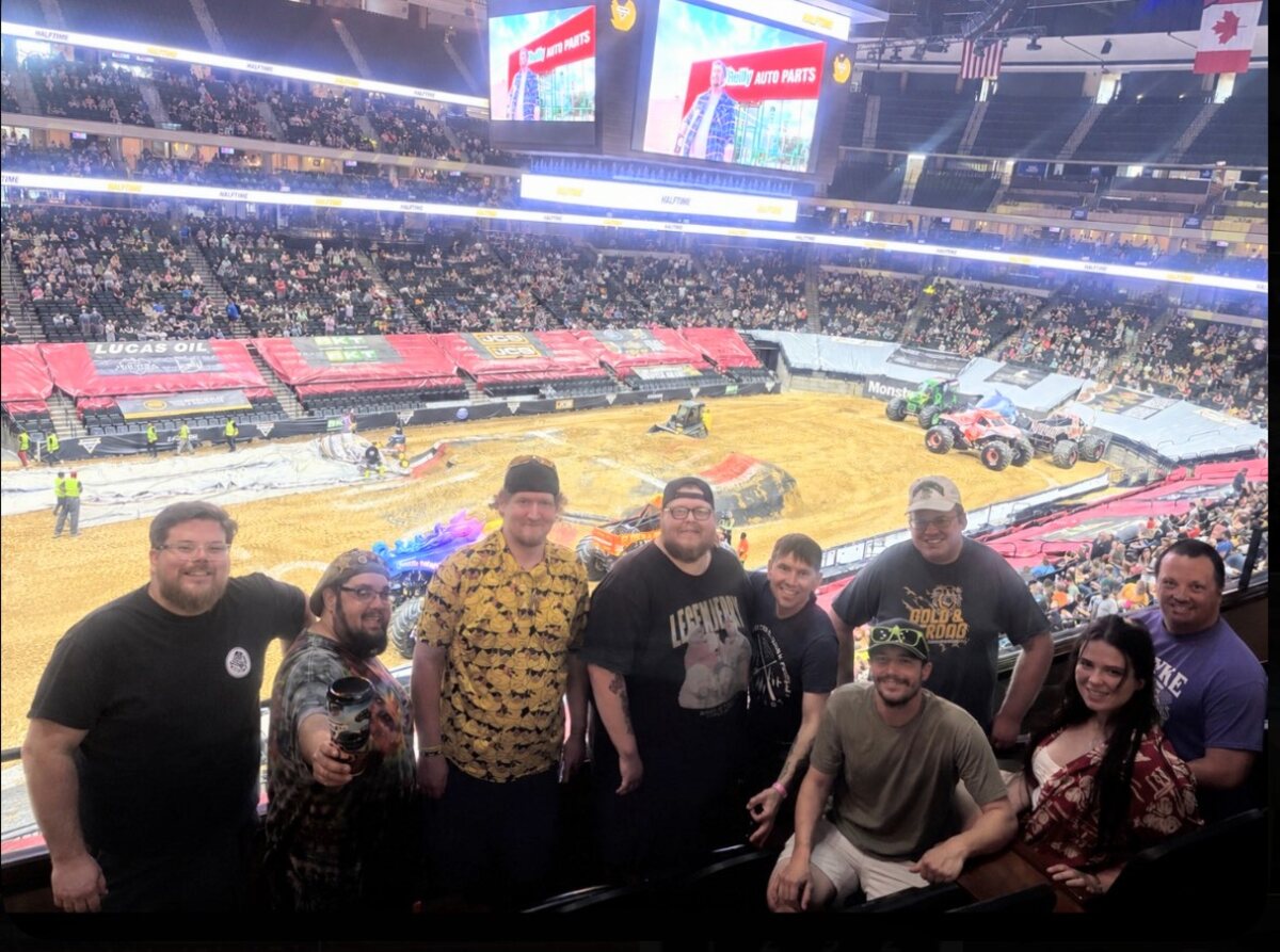 The whole Monster Jam crew lined up in the suite with the dirt track and packed arena behind them