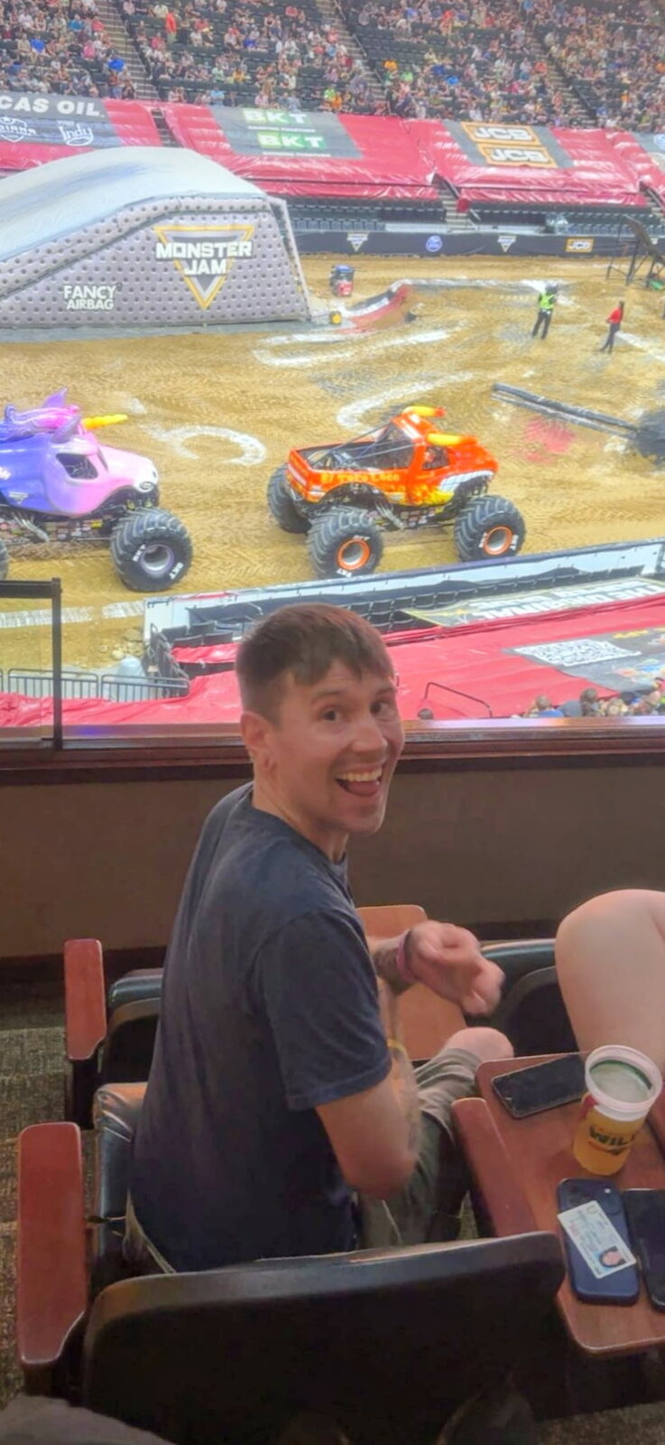 Josh grinning back at the camera from his suite seat as monster trucks roll out onto the dirt below