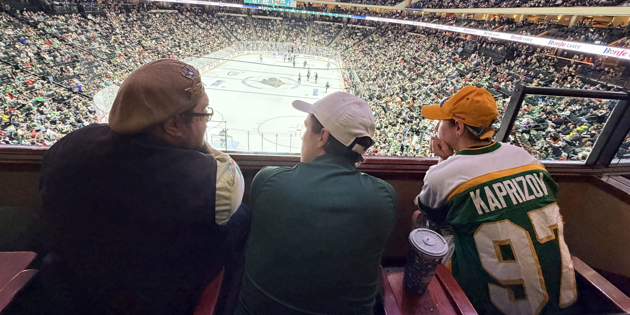 Three friends in the suite watching the Wild play from above the ice, with a packed arena all around