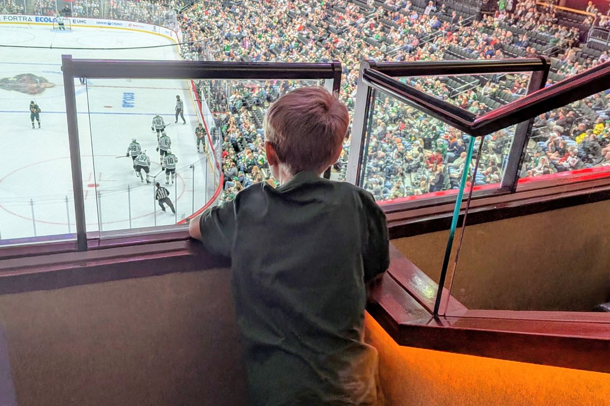 A young boy leaning on the suite glass to watch the game on the ice below