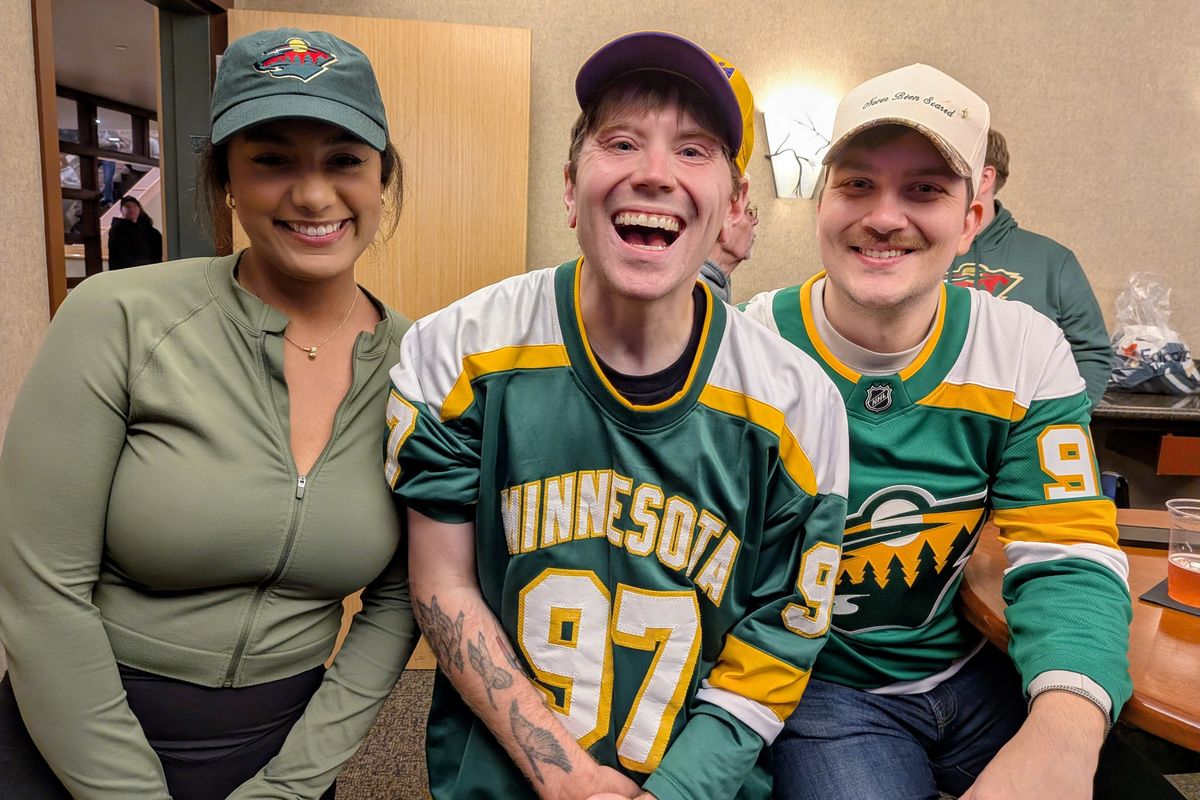 Three friends laughing together in the suite, one in a green and gold number 97 jersey